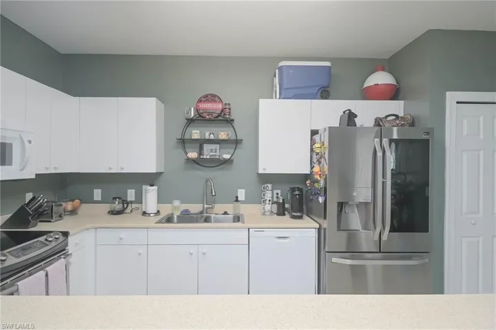 Kitchen featuring stainless steel appliances, light countertops, and white cabinets