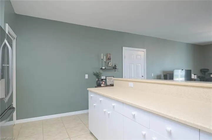 Kitchen with stainless steel fridge, light tile patterned flooring, white cabinetry, and light stone counters