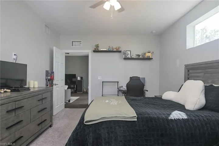 Bedroom with light carpet, a ceiling fan, and an office area