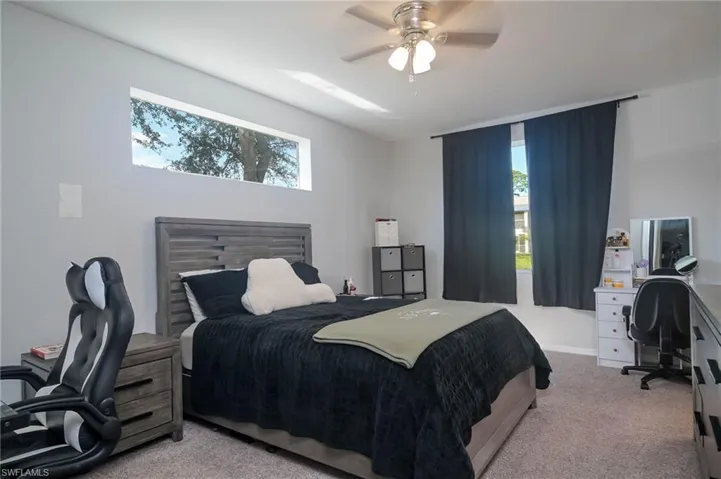 Bedroom with a desk, light colored carpet, and a ceiling fan