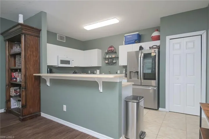 Kitchen featuring stainless steel fridge, a kitchen breakfast bar, white cabinets, a peninsula, and light countertops