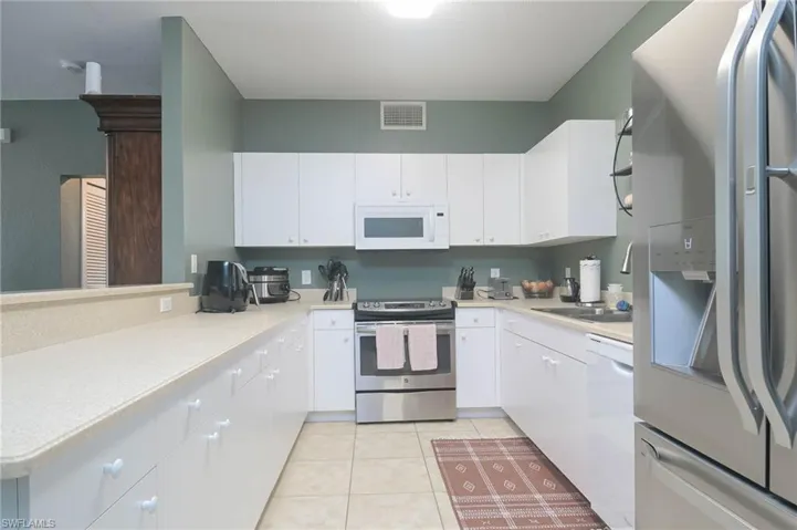 Kitchen with white appliances, light tile patterned floors, and white cabinets