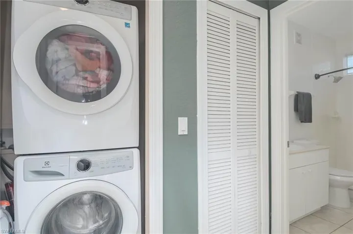 Washroom featuring stacked washer / drying machine and light tile patterned floors