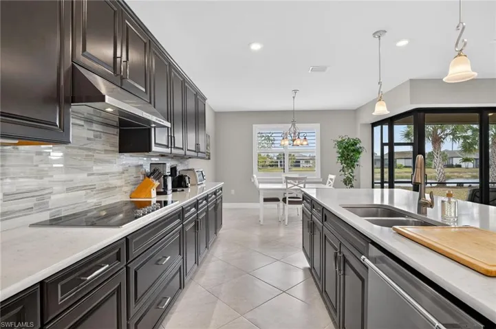 Kitchen with pendant lighting, light stone counters, dishwasher, black electric cooktop, and decorative backsplash