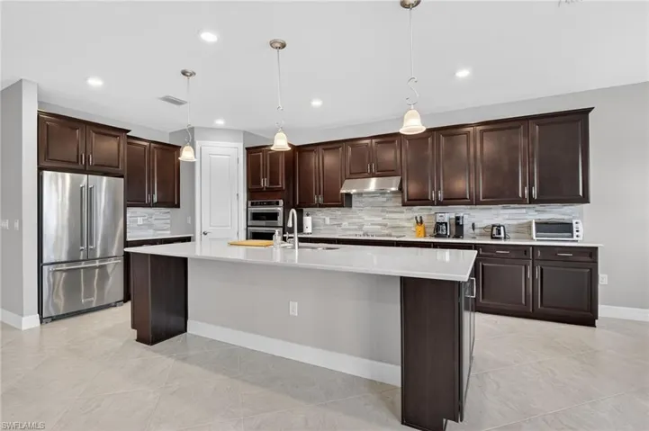Kitchen featuring dark wood finish cabinetry, stainless steel appliances, pendant lighting, and an island with sink