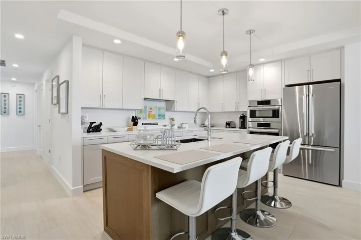 Kitchen featuring stainless steel appliances, white cabinetry, a kitchen breakfast bar, and recessed lighting - Virtually Edited Image