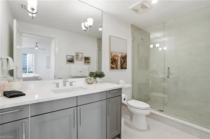 Ensuite bathroom with vanity, a stall shower, a chandelier, a ceiling fan, and light tile patterned flooring - Virtually Edited Image