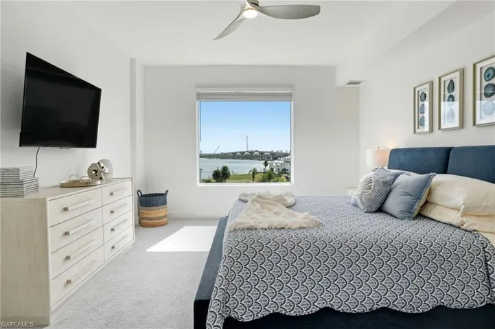 Bedroom featuring light carpet, ceiling fan, and a water view - Virtually Edited Image