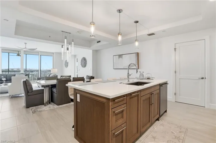 Kitchen featuring a tray ceiling, pendant lighting, open floor plan, and a center island with sink - Virtually Edited Image