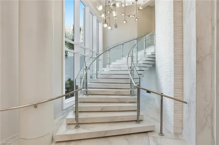 Stairway of Lobby featuring marble finish floors and a chandelier- Virtually Edited