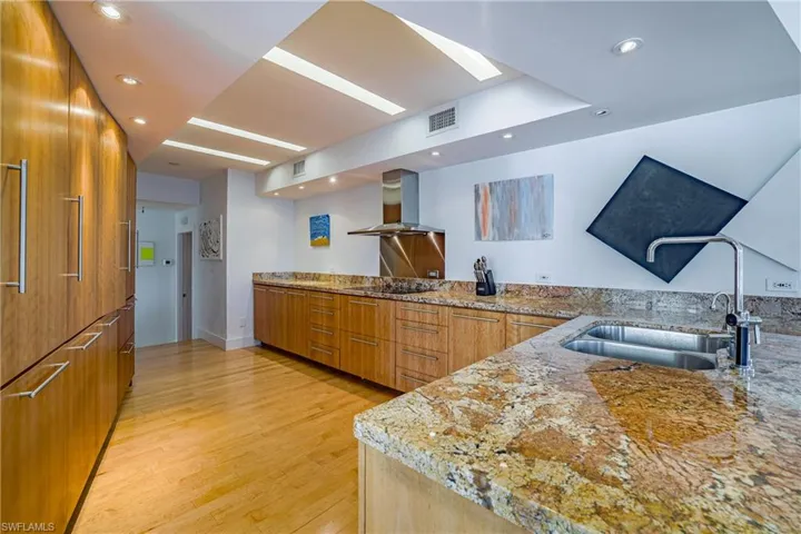 Kitchen featuring brown cabinetry, light stone countertops, modern cabinets, wall chimney exhaust hood, and recessed lighting