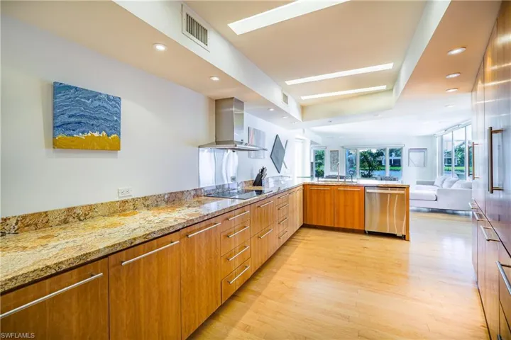 Kitchen with modern cabinets, open floor plan, light stone counters, range hood, and light wood-style floors