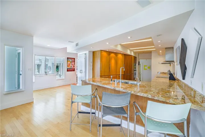 Kitchen featuring brown cabinets, a kitchen bar, light stone counters, a peninsula, and recessed lighting