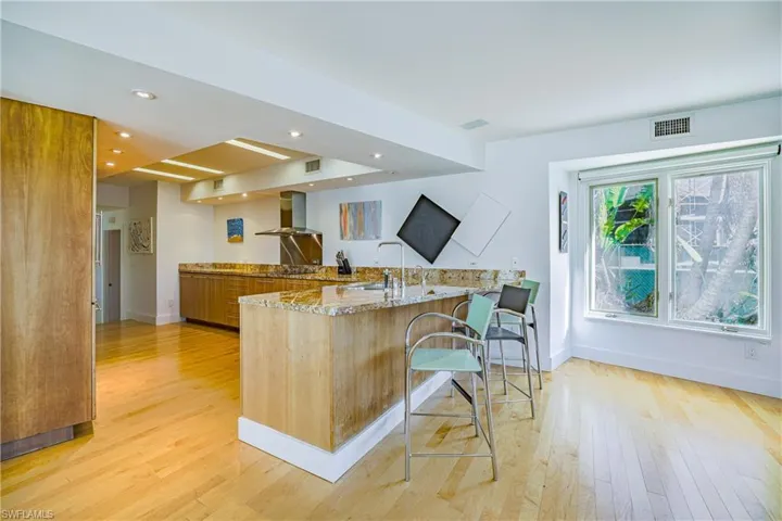 Kitchen featuring light stone countertops, a peninsula, recessed lighting, a breakfast bar, and wall chimney exhaust hood