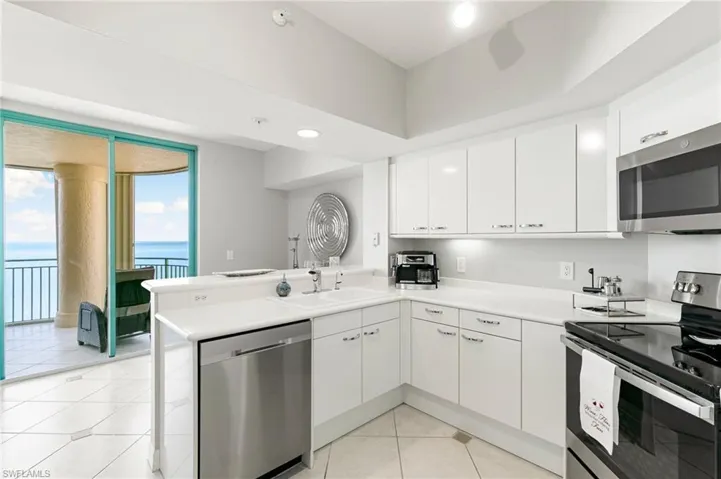 Kitchen with stainless steel appliances, white cabinets, light tile patterned floors, sink, and kitchen peninsula