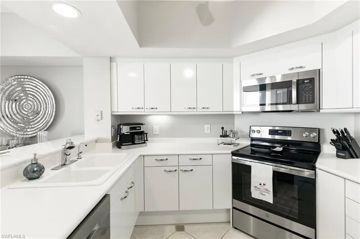 Kitchen with light tile patterned flooring, appliances with stainless steel finishes, sink, and white cabinetry