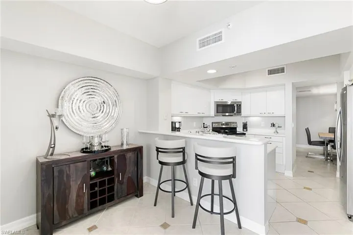 Kitchen featuring a breakfast bar, light tile patterned flooring, appliances with stainless steel finishes, white cabinetry, and kitchen peninsula