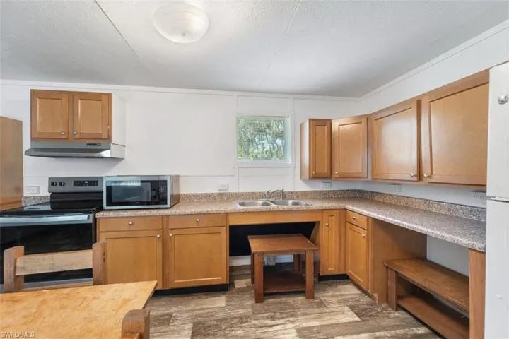 Kitchen featuring appliances with stainless steel finishes, under cabinet range hood, a sink, wood finished floors, and light countertops