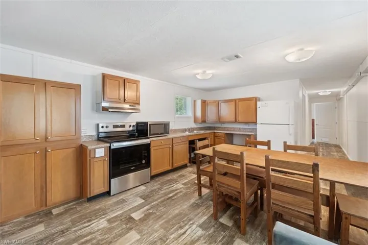 Kitchen featuring appliances with stainless steel finishes, under cabinet range hood, wood finished floors, light countertops, and brown cabinets