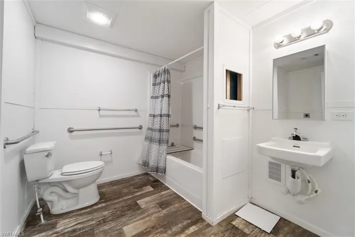 Bathroom featuring toilet, wood finished floors, shower / bath combo, a sink, and baseboards