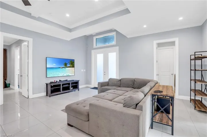 Living room with light tile patterned flooring, french doors, a tray ceiling, and ornamental molding
