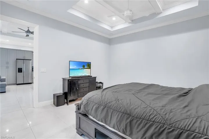 Tiled bedroom with stainless steel refrigerator with ice dispenser, coffered ceiling, ceiling fan, and crown molding