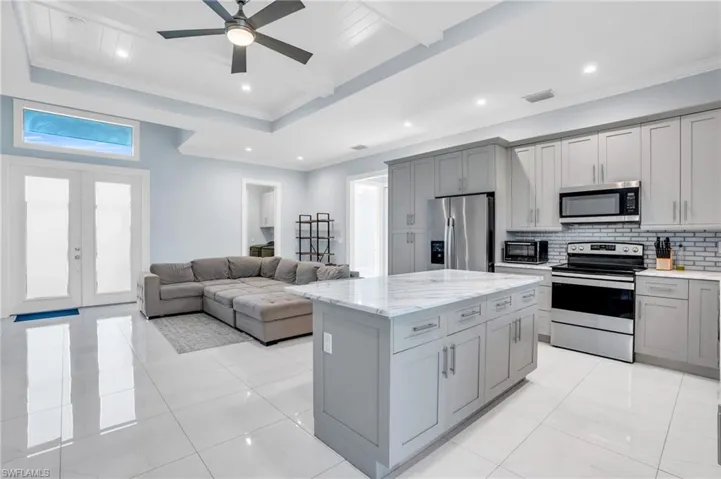 Kitchen featuring french doors, a kitchen island, ceiling fan, stainless steel appliances, and decorative backsplash