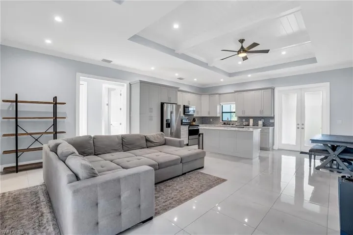 Tiled living room featuring crown molding, a tray ceiling, french doors, and ceiling fan