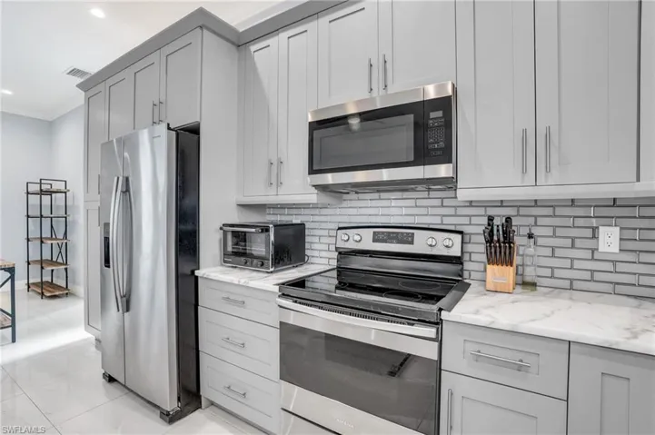 Kitchen with backsplash, light tile patterned floors, light stone counters, and stainless steel appliances