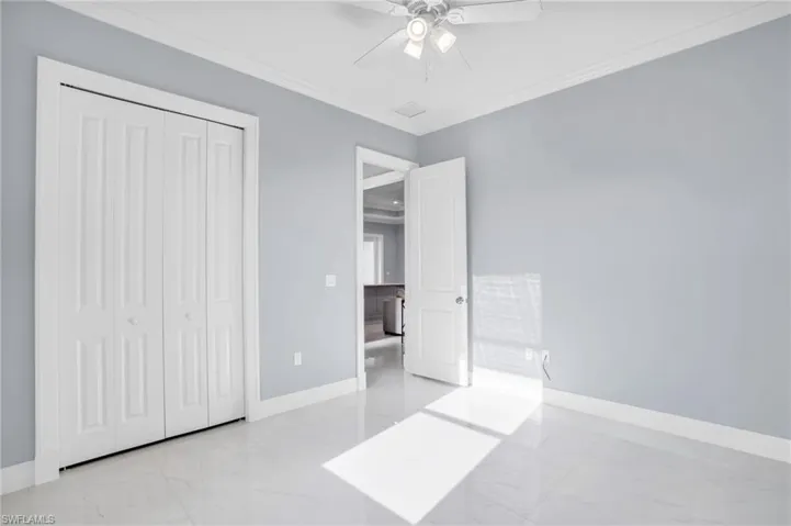 Unfurnished bedroom featuring light tile patterned flooring, a closet, ornamental molding, and ceiling fan