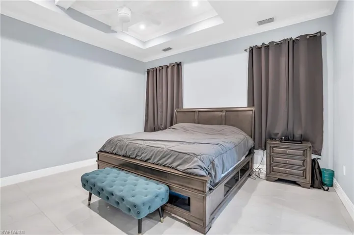 Bedroom with ornamental molding, light tile patterned flooring, ceiling fan, and a raised ceiling