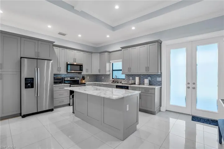 Kitchen with stainless steel appliances, gray cabinetry, french doors, backsplash, and light stone countertops