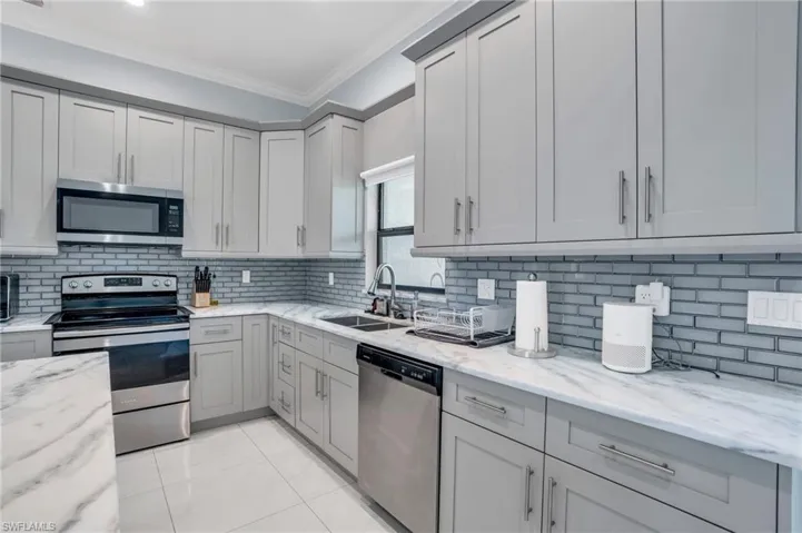 Kitchen with gray cabinetry, sink, stainless steel appliances, and backsplash