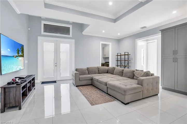 Tiled living room with a tray ceiling, french doors, and ornamental molding