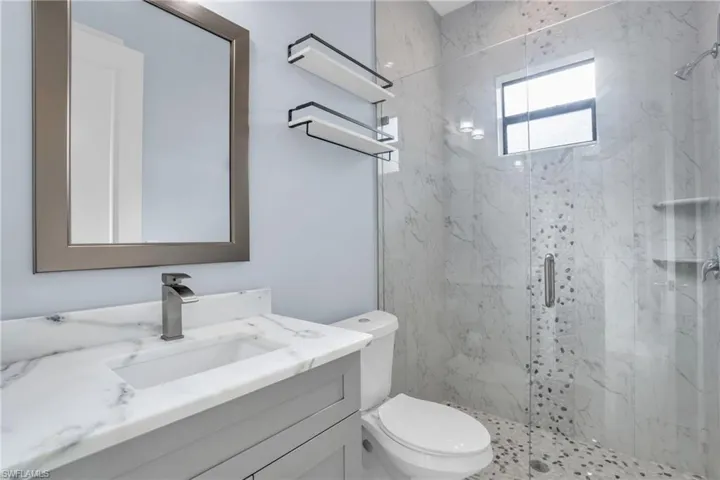 Bathroom featuring a shower with door, toilet, and vanity