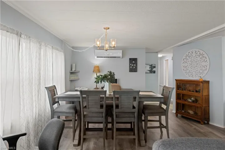 Dining room with crown molding, vinyl flooring, a notable chandelier, and an AC wall unit