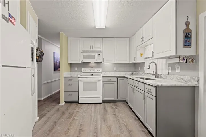 Kitchen with vinyl flooring, gray cabinets, white cabinets, sink, and white appliances