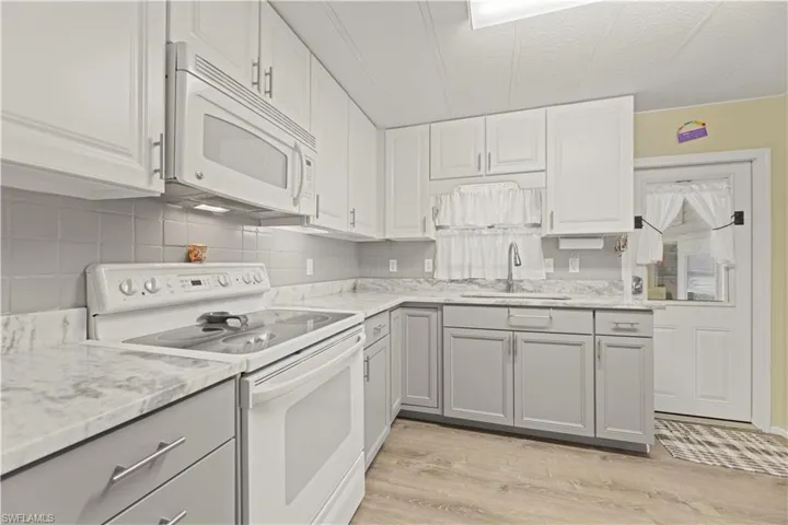 Kitchen with light wood-type vinyl flooring, white appliances, gray cabinets, sink, and tasteful backsplash