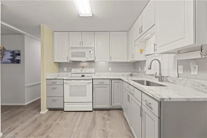 Kitchen featuring tasteful backsplash, white cabinetry, light wood-type flooring, sink, and white appliances