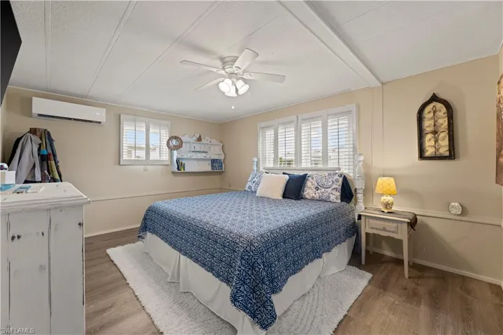 Bedroom with vinyl/ wood-style flooring, multiple windows, ceiling fan, and an AC wall unit