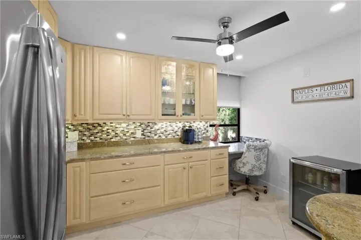 Kitchen featuring freestanding refrigerator, light wood finish cabinets, glass insert cabinets, light stone countertops, and backsplash