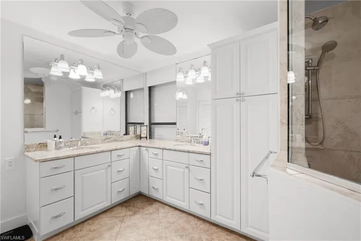 Full bath with double vanity, a marble finish shower, ceiling fan, and light tile patterned floors