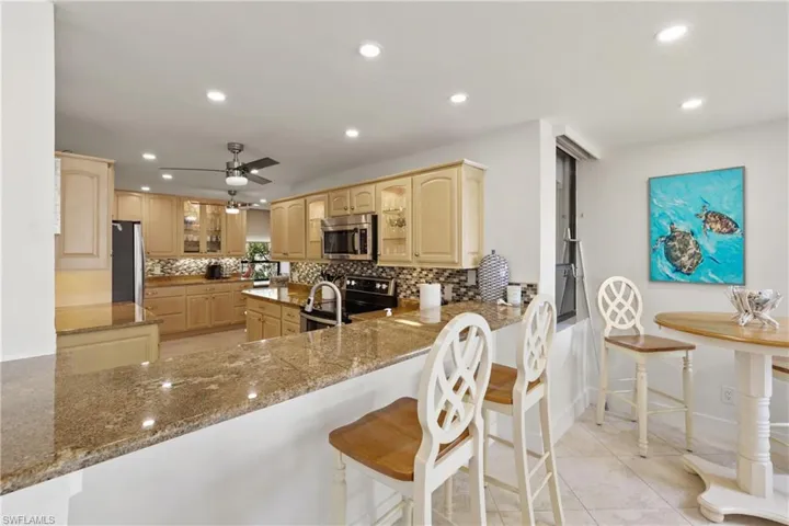 Kitchen with dark stone countertops, tasteful backsplash, a peninsula, a breakfast bar area, and recessed lighting