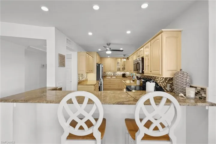 Kitchen with light wood finish cabinetry, stainless steel appliances, tasteful backsplash, a peninsula, and a ceiling fan