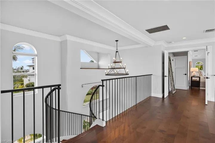 Hallway featuring ornamental molding, dark wood-style flooring, suspended lighting, and an upstairs landing