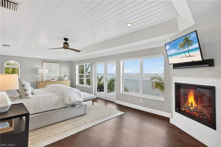 Bedroom with access to outside, wood-type flooring, a wood tray ceiling, a ceiling fan, and a fireplace
