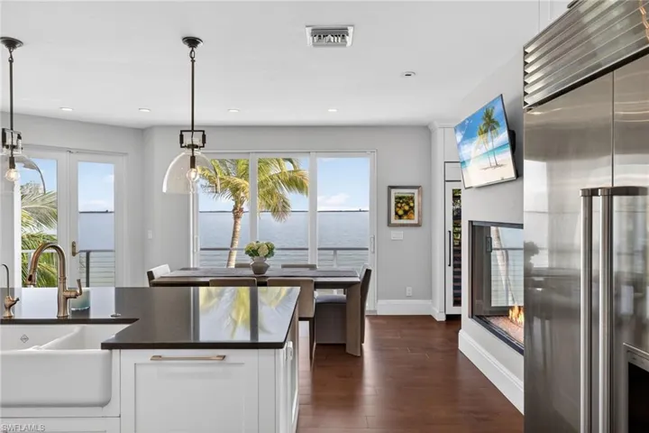 Kitchen with white cabinets, stainless steel built in fridge, hanging light fixtures, dark wood-type flooring, and dark stone counters