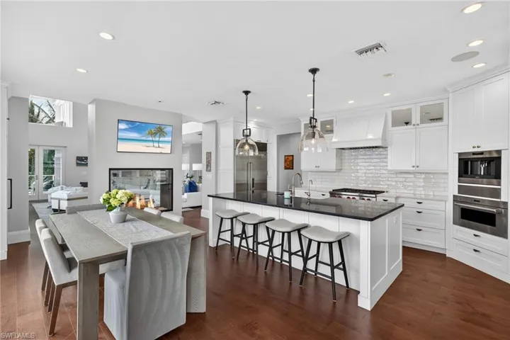 Kitchen featuring a breakfast bar, an island with sink, white cabinets, dark stone countertops, and decorative light fixtures