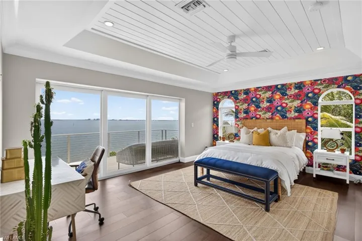 Bedroom featuring a water view, access to exterior, dark wood-type flooring, a ceiling fan, and a desk