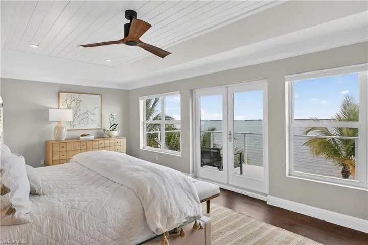Bedroom featuring access to exterior, hardwood / wood-style floors, a wood tray ceiling, a ceiling fan, and a water view